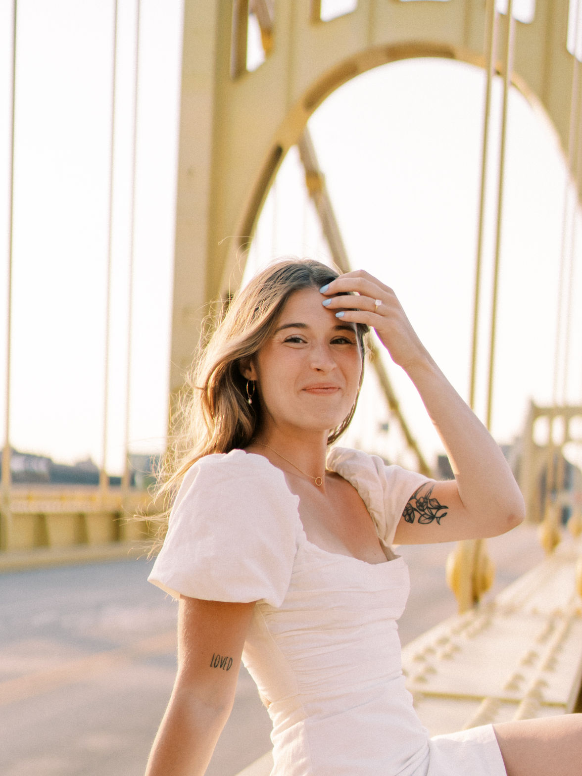 Ashley sitting on a yellow suspension bridge in warm backlight, pushing her hair back from her face.